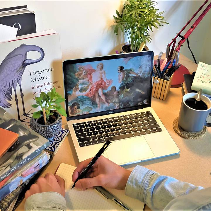 Person writing at desk with laptop and books on